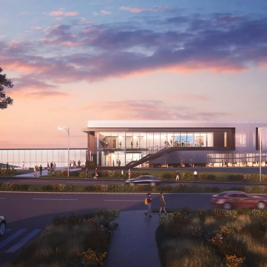 Modern glass building at sunset with cars and people on the road and natural landscaping around.