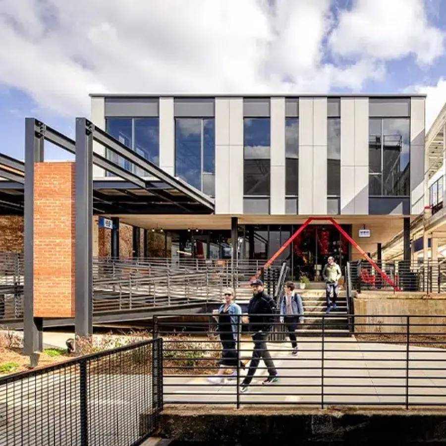 Modern industrial building with metal beams and brick walls, people walking outside under a blue sky.