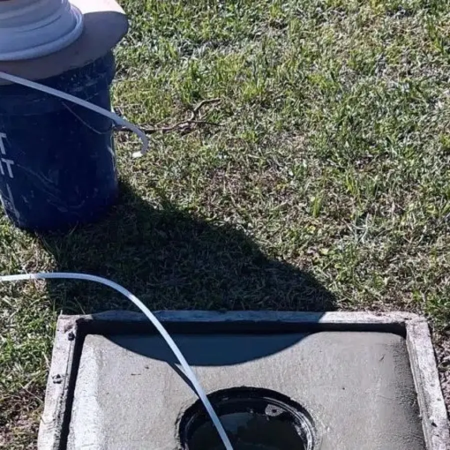 Concrete pad with circular opening and a spool of white tubing on grass outdoors in sunlight.
