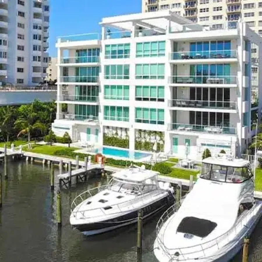Luxury waterfront apartments with docks and yachts by a calm marina under a clear blue sky.