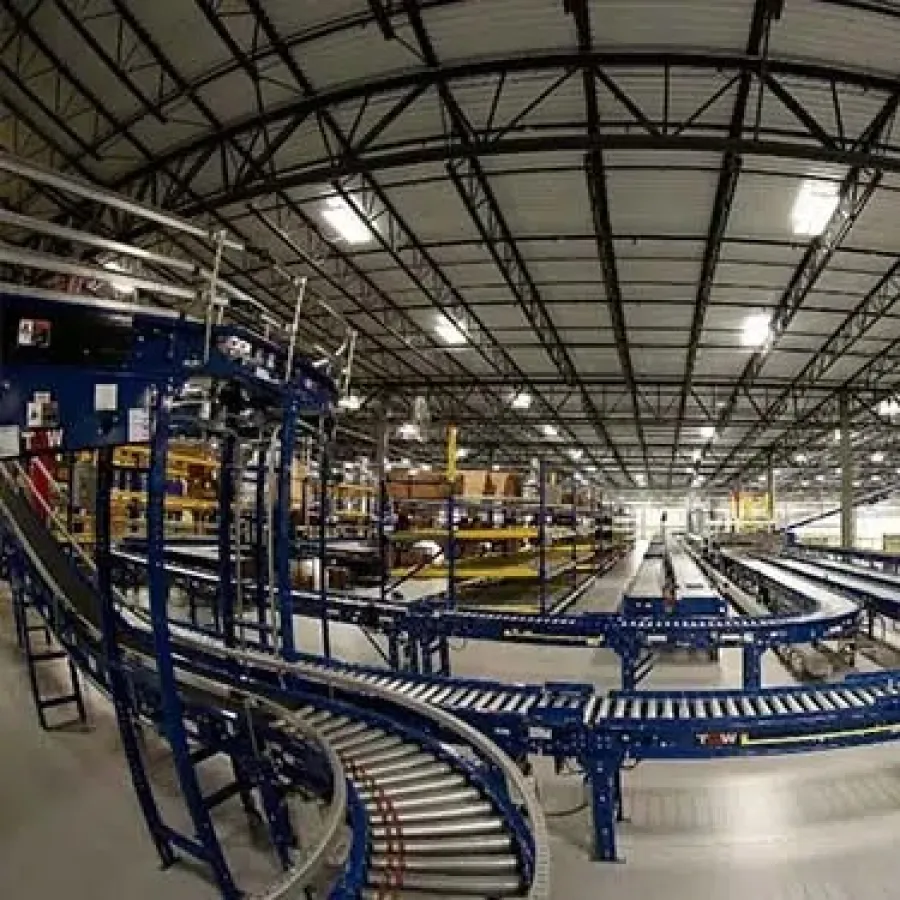 Wide view of an industrial warehouse with blue conveyor belts, yellow shelving, and overhead lighting.