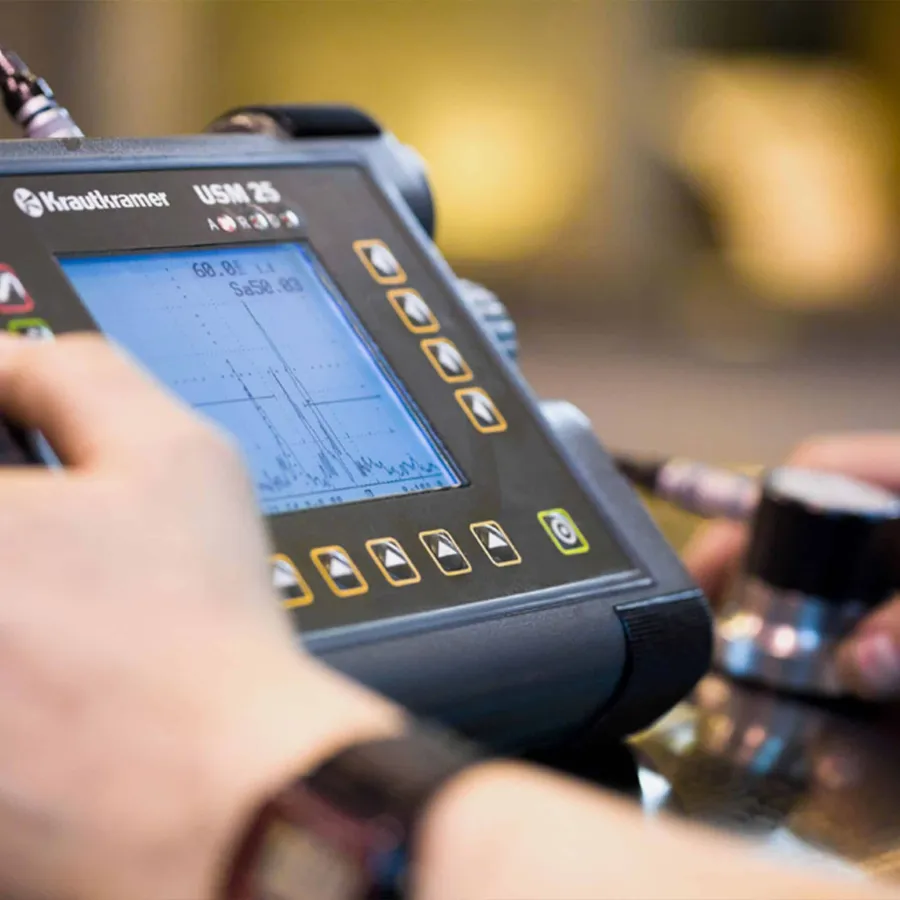 Hand holding probe connected to Krautkramer USM 25 ultrasonic testing device with graph display