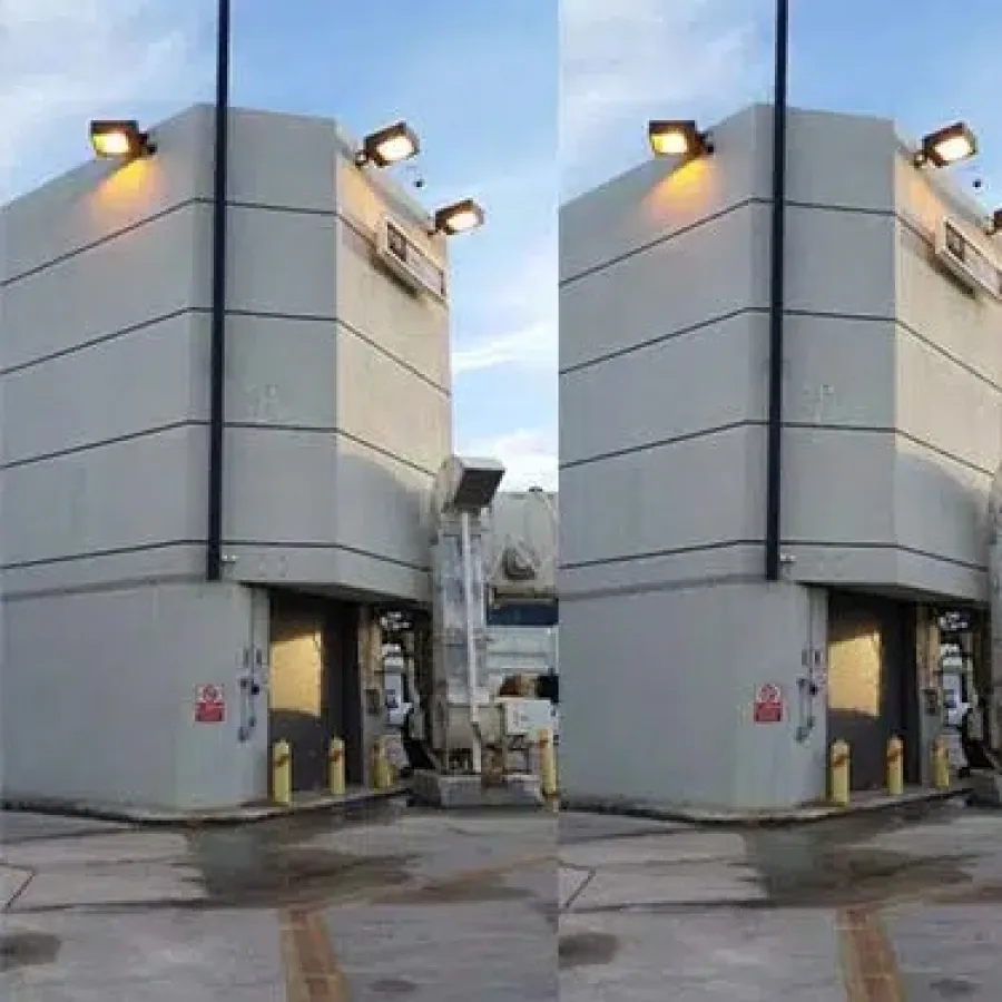 Exterior of a modern industrial building with security lights and a loading dock under a blue sky.
