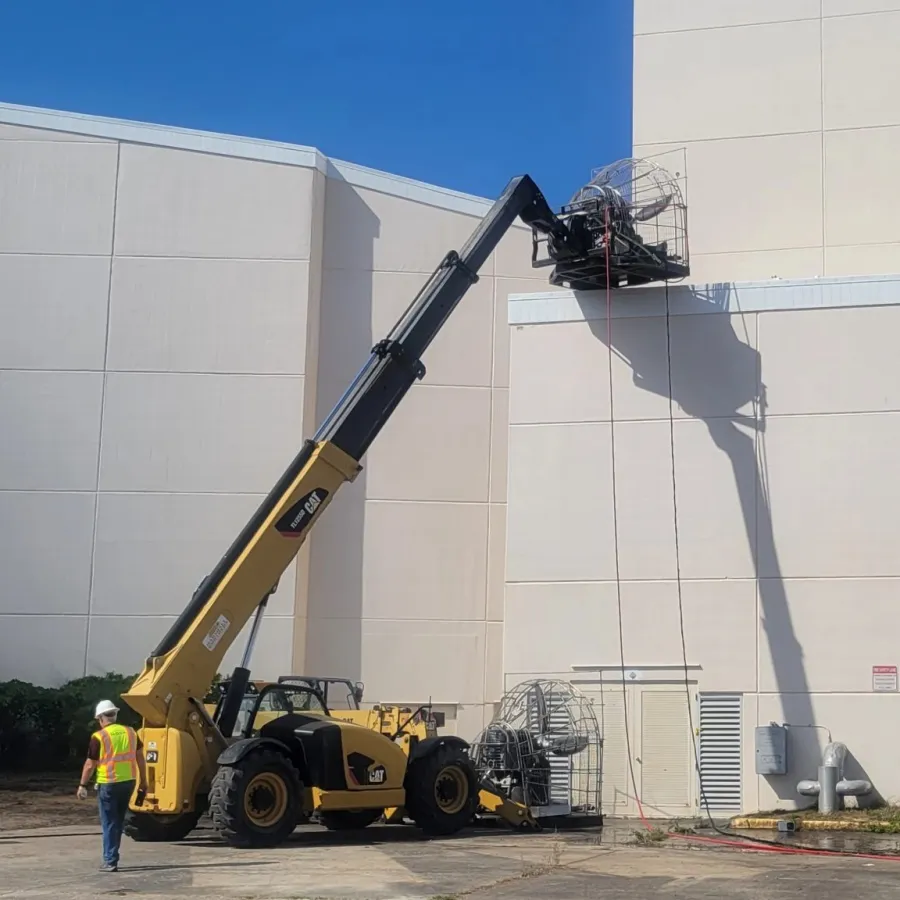 Construction workers using a yellow telescopic forklift to access the top of a beige industrial building on a sunny day