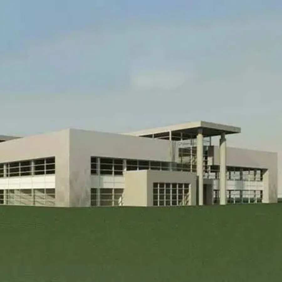 Modern industrial building with large windows and flat roof surrounded by grassy landscape under clear sky