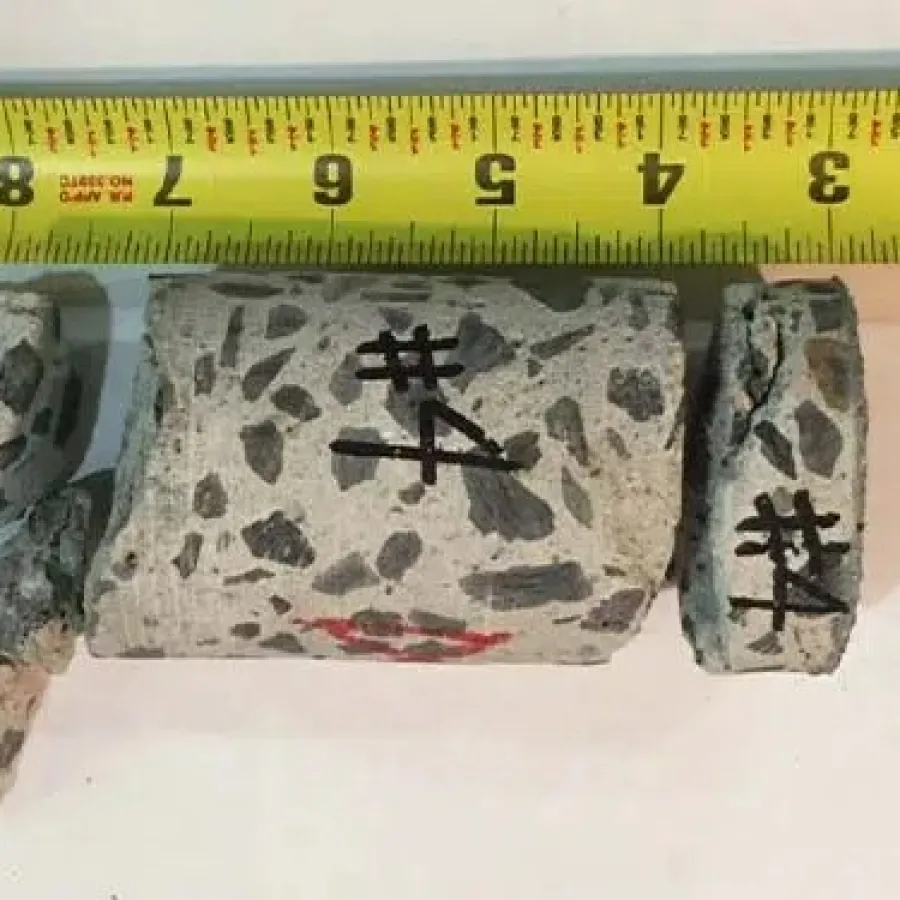 Broken concrete test samples with black markings and a measuring tape showing length above them.