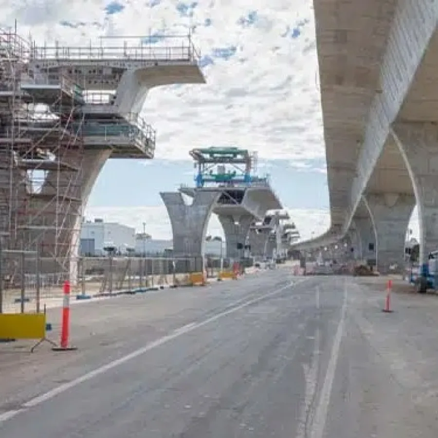 Construction site of elevated concrete highway or rail bridge with scaffolding and machinery under partly cloudy sky.