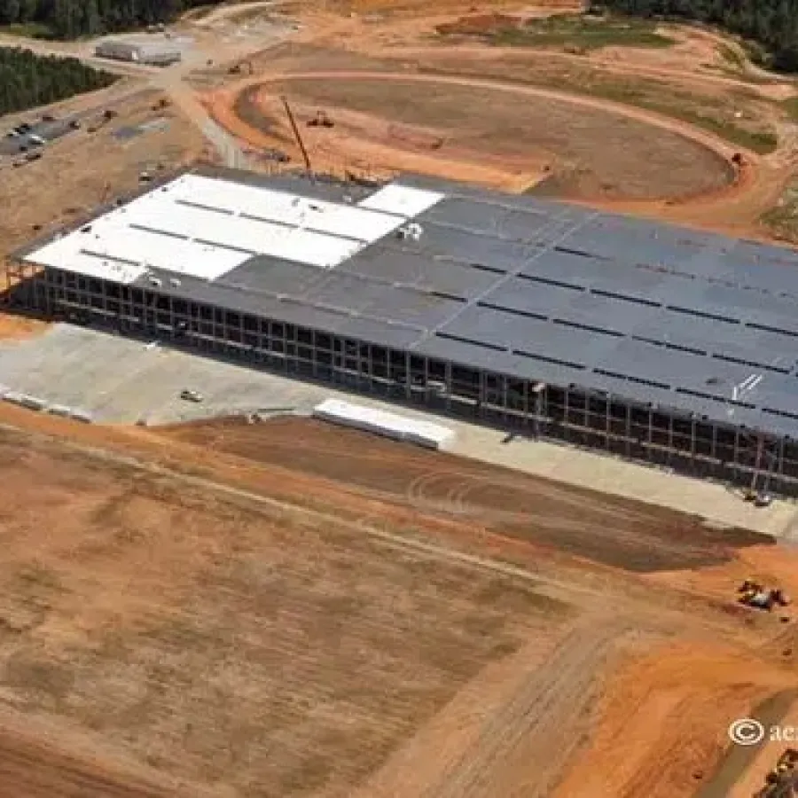 Aerial view of a large warehouse under construction surrounded by cleared red dirt and forested area