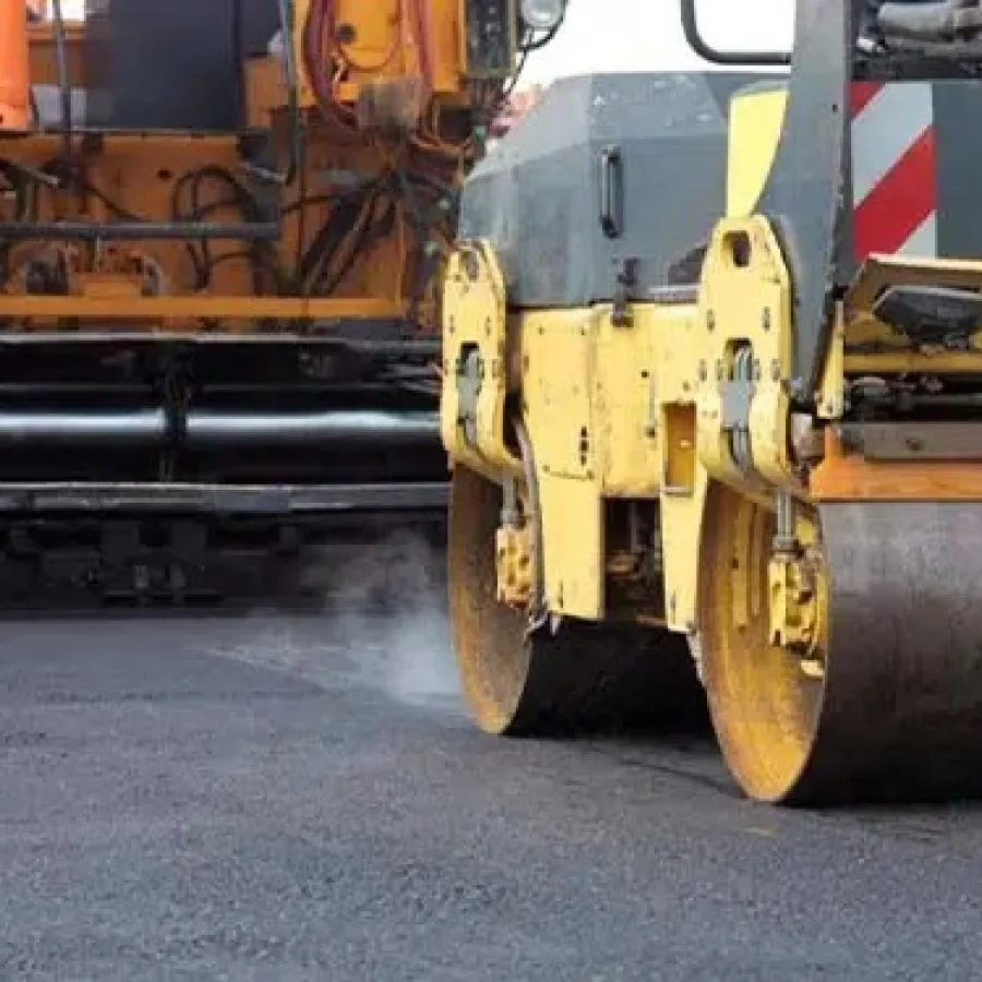Yellow road roller machine compacting freshly laid asphalt on a street construction site.