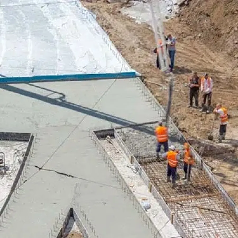 Construction workers pouring and smoothing concrete on a large paved area at a construction site.