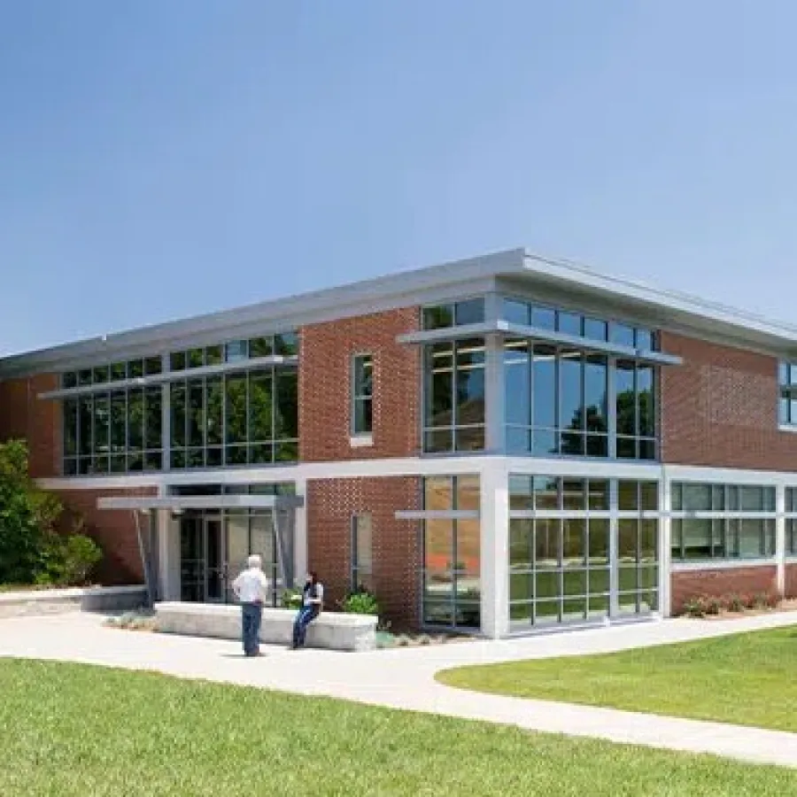 Modern two-story brick office building with large windows, surrounded by green lawn and small trees under a clear sky.