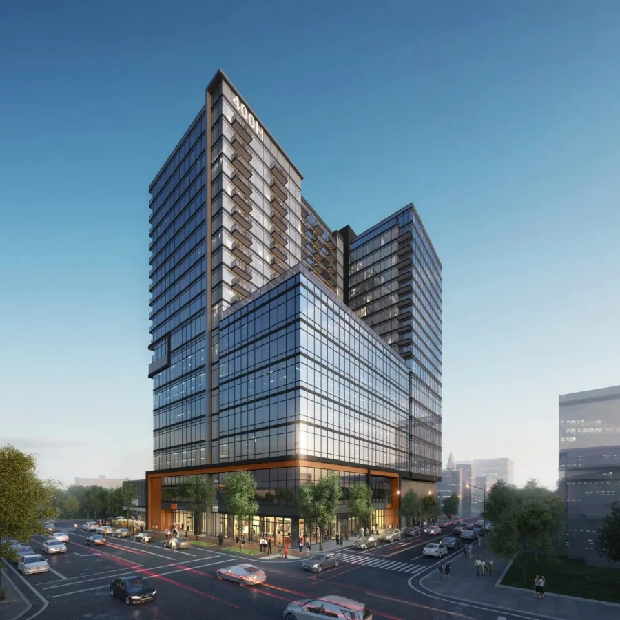 Modern glass office building with urban street, cars, trees, and pedestrians under clear sky at sunset.