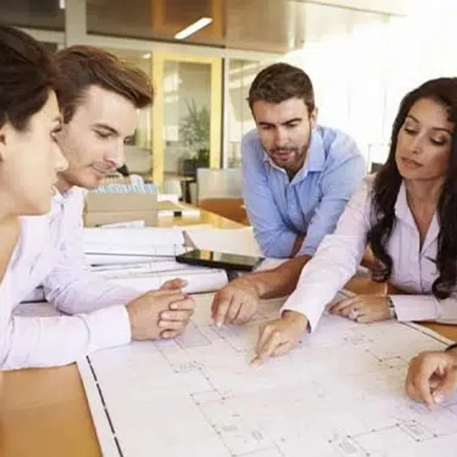 Team of five professionals collaborating over blueprints in modern office during meeting.