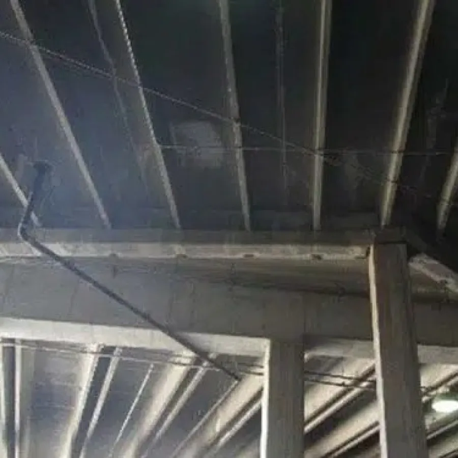 Concrete ceiling with exposed beams and pipes in an industrial or parking garage setting under dim lighting