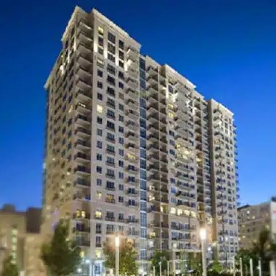 Tall residential building with lit windows at dusk against a clear blue sky in an urban setting.