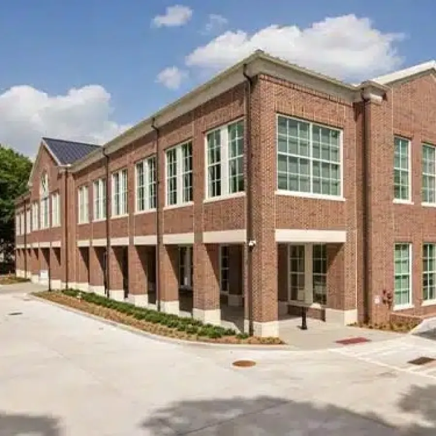 Modern two-story red brick office building with large windows under a blue sky with white clouds