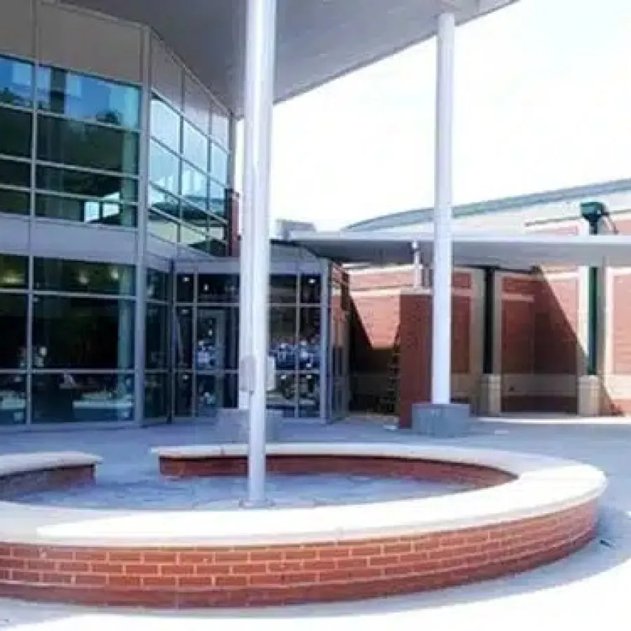 Modern school entrance with circular brick planter, glass doors, and covered walkway under bright daylight.