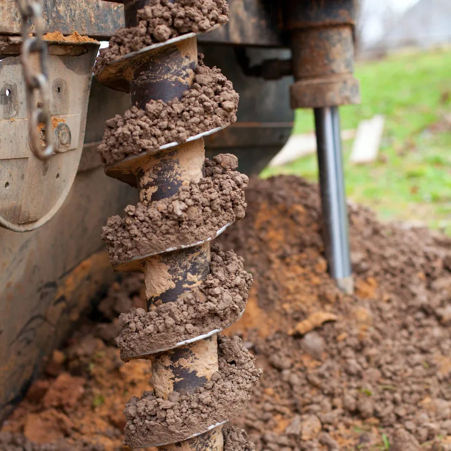 Close-up of a mud-covered auger drill bit attached to heavy machinery at a construction site.