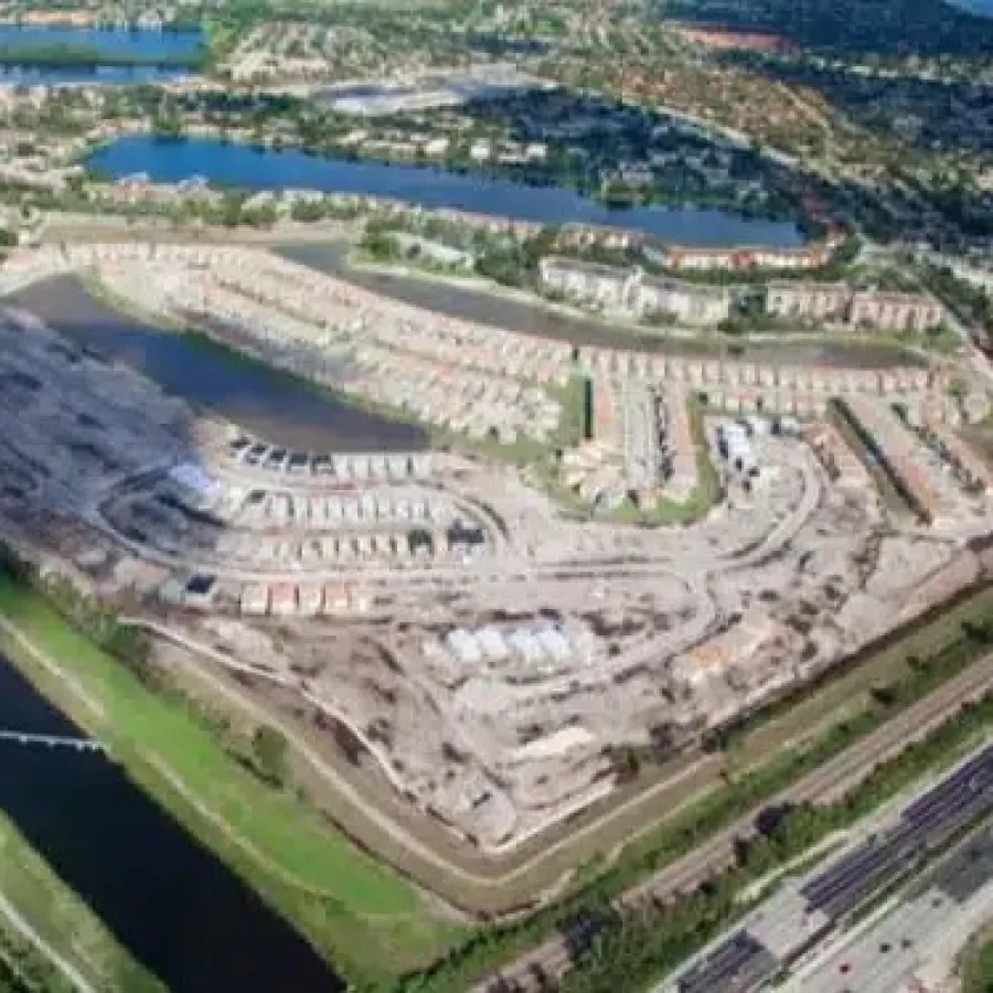 Aerial view of a large residential construction site surrounded by canals and a highway in a suburban area.
