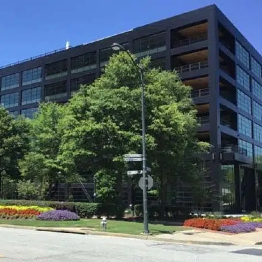 Modern office building with large windows surrounded by trees and colorful flower beds on a sunny day