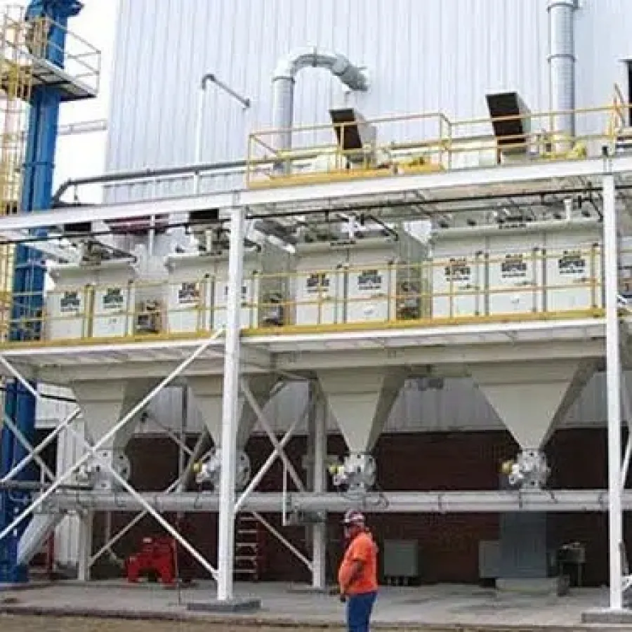 Industrial facility with six large white silos supported by metal framework and two workers in safety gear nearby.