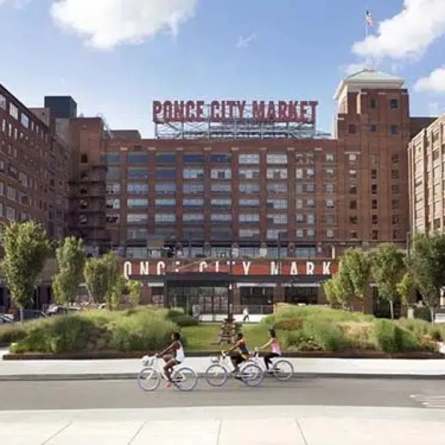 Exterior view of historic Ponce City Market with people biking and a motorbike on the street in a sunny urban scene