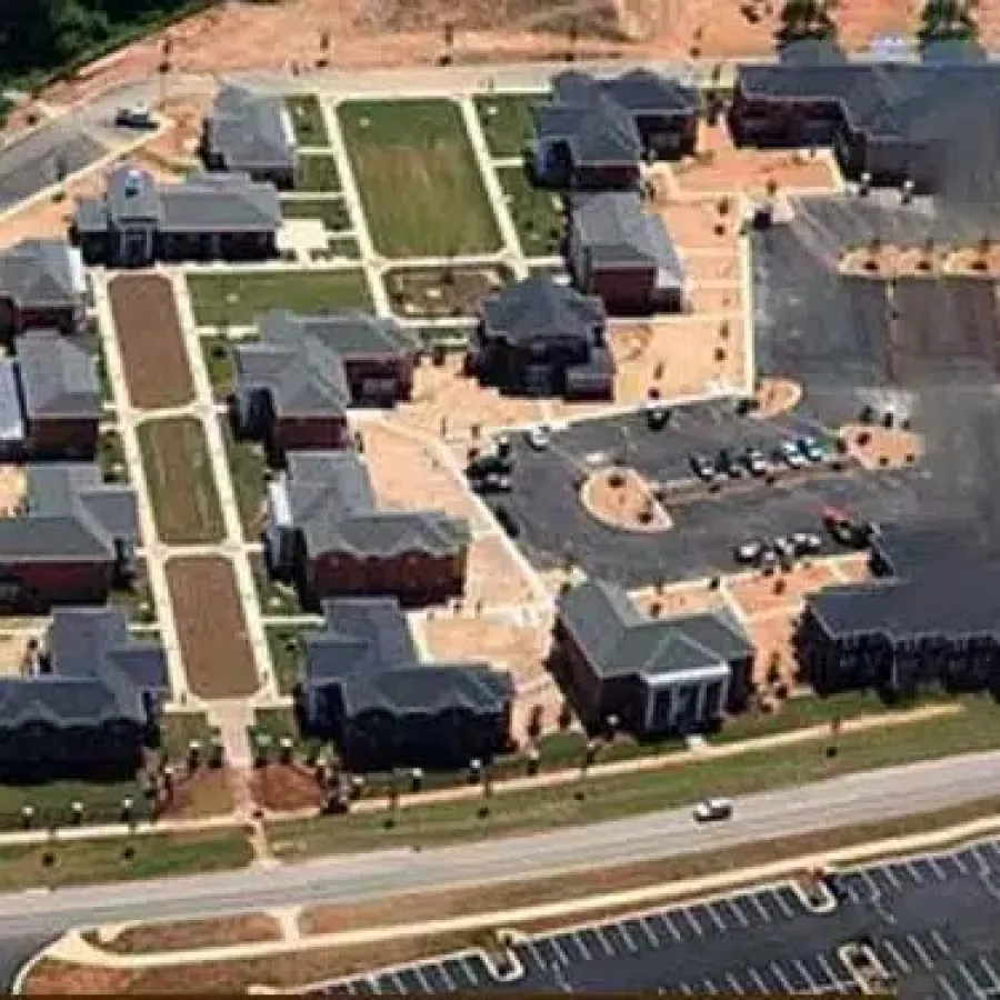 Aerial view of a campus-style housing complex with multiple buildings, green lawns, and parking lots under sunlight.