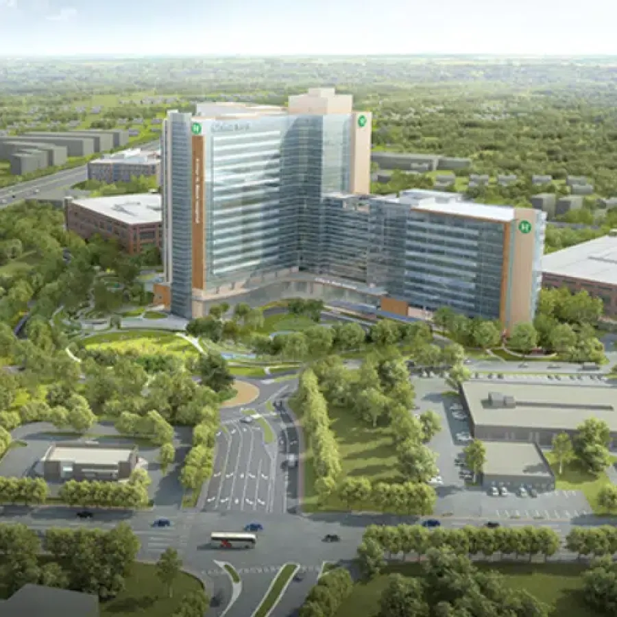 Aerial view of a modern medical complex surrounded by greenery and roads under a clear sky.