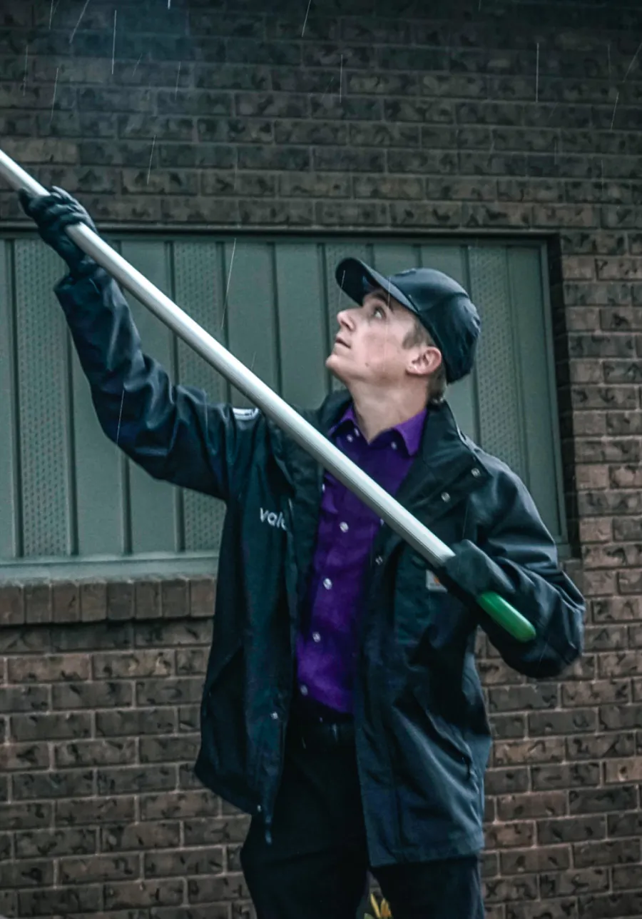 Worker in rain gear holding a long pole looking upward against a brick wall background