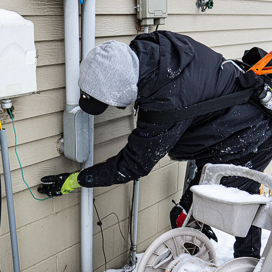 Technician in winter gear working on an outdoor electrical panel during snowy weather.