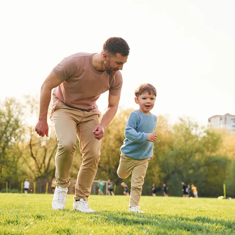 Father and son running and playing together on a sunny grassy field with trees in the background