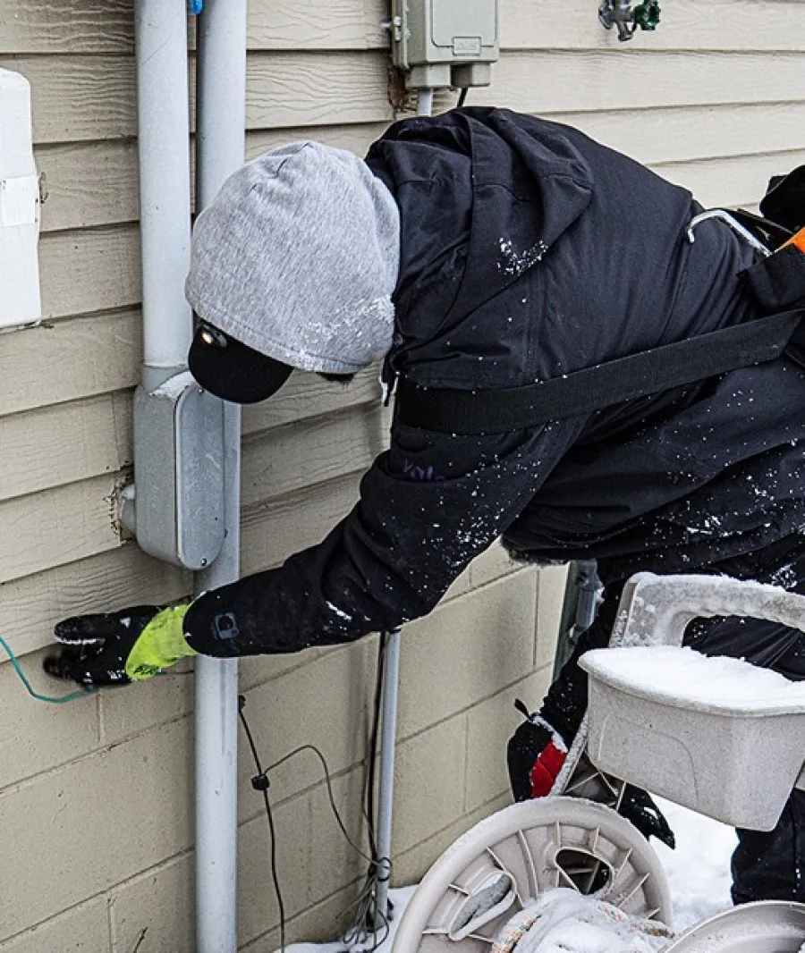 Technician in winter gear working on an outdoor electrical panel during snowy weather.