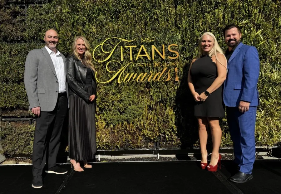 Four people dressed formally stand on a stage in front of a green wall with MSP Titans of the Industry Awards sign.
