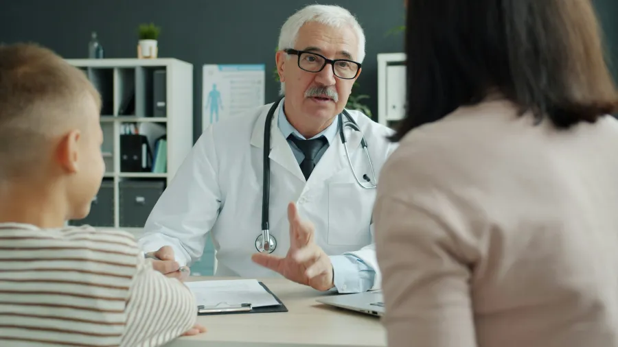 Senior male doctor explaining health information to a woman and child in a medical office consultation.