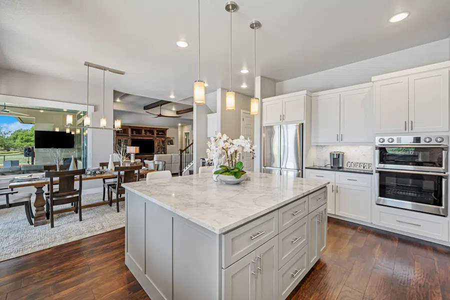 Modern open kitchen with marble island, white cabinets, stainless steel appliances, and adjacent dining area with wooden table.