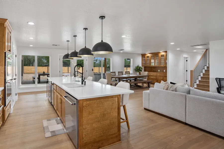 Spacious open kitchen and living area with wooden cabinetry, white countertops, modern pendant lights, and light hardwood floors.