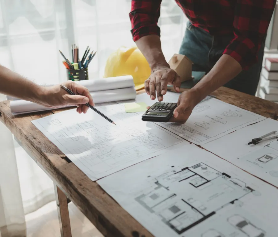 Architects working on building plans with calculator and pencil on wooden table in bright office.