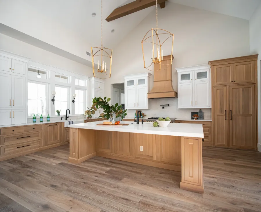 Spacious modern kitchen with large wooden island, white countertops, pendant lights, and natural wood cabinetry.