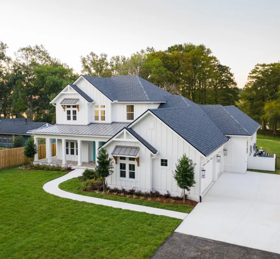 Modern two-story white house with a dark roof, spacious front yard, and a curved driveway in a suburban area.