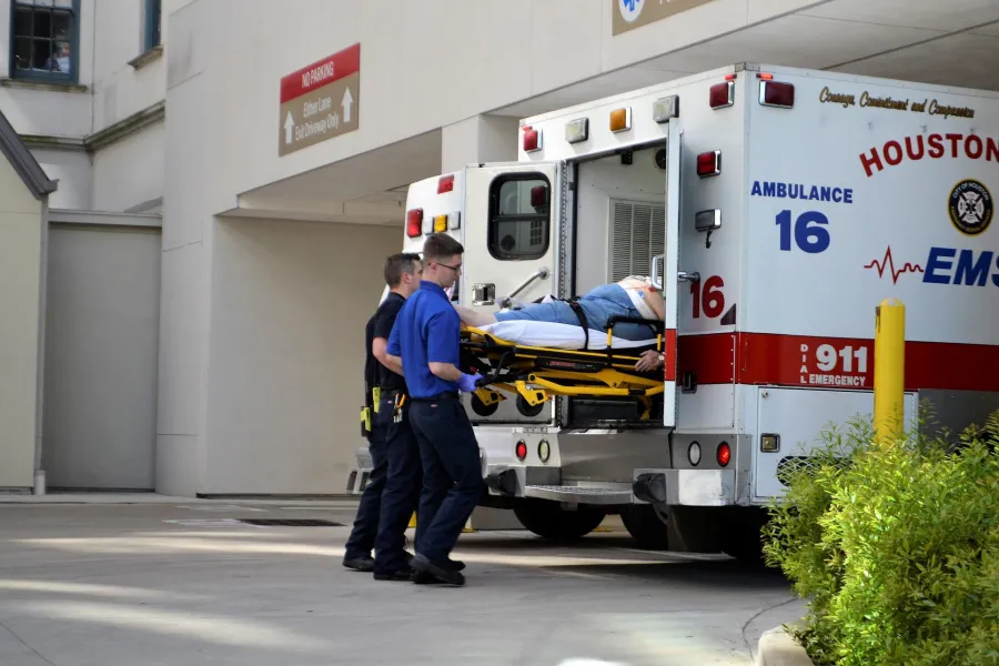 Emergency medical staff loading a patient into a Houston ambulance outside a hospital.