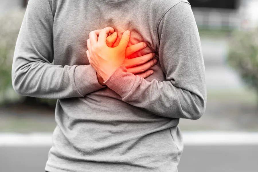 Person clutching chest in pain, suggesting heart issues or discomfort outdoors.