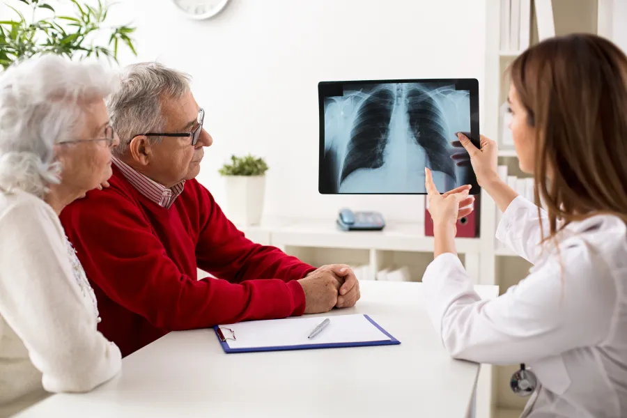 Doctor explaining X-ray results to elderly couple in a modern medical office setting.