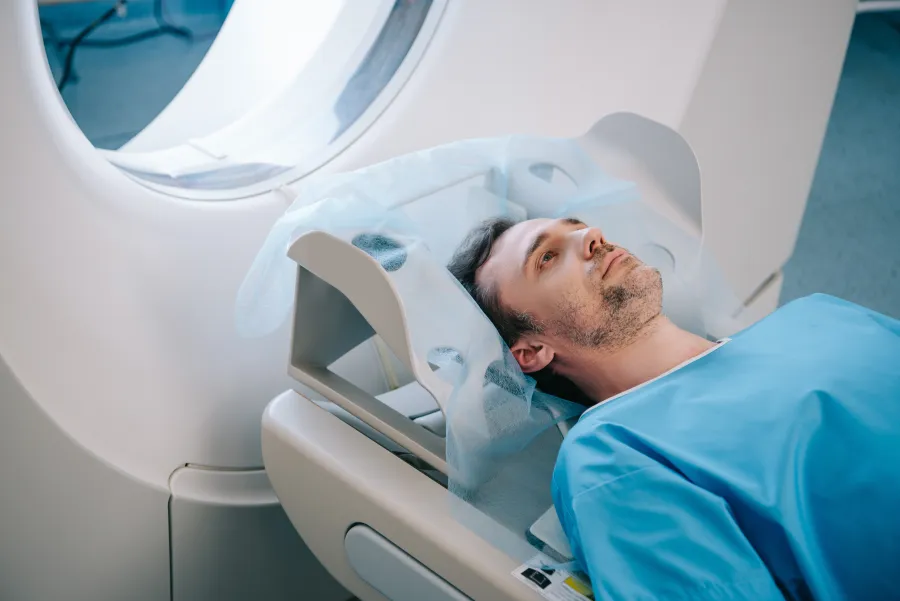 Patient preparing for a CT scan, wearing a gown and lying on the scanner bed.