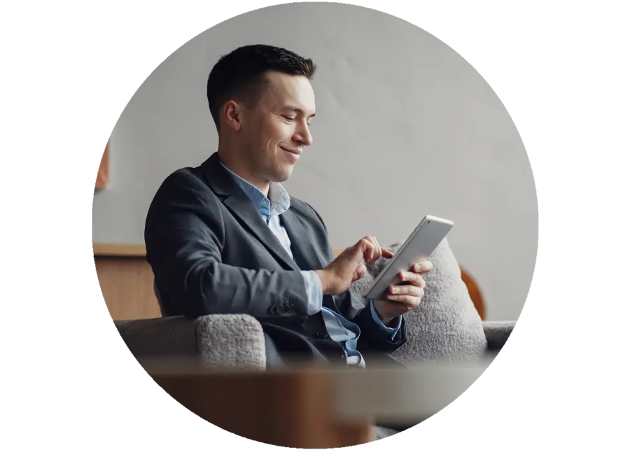 Smiling businessman in suit using tablet while sitting on a cozy armchair indoors