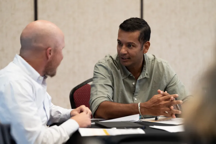 Two men engaged in a focused discussion at a table with documents and a laptop in a professional setting
