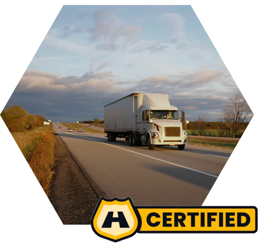 White semi-truck driving on a highway with cloudy sky and autumn landscape, certified badge included.