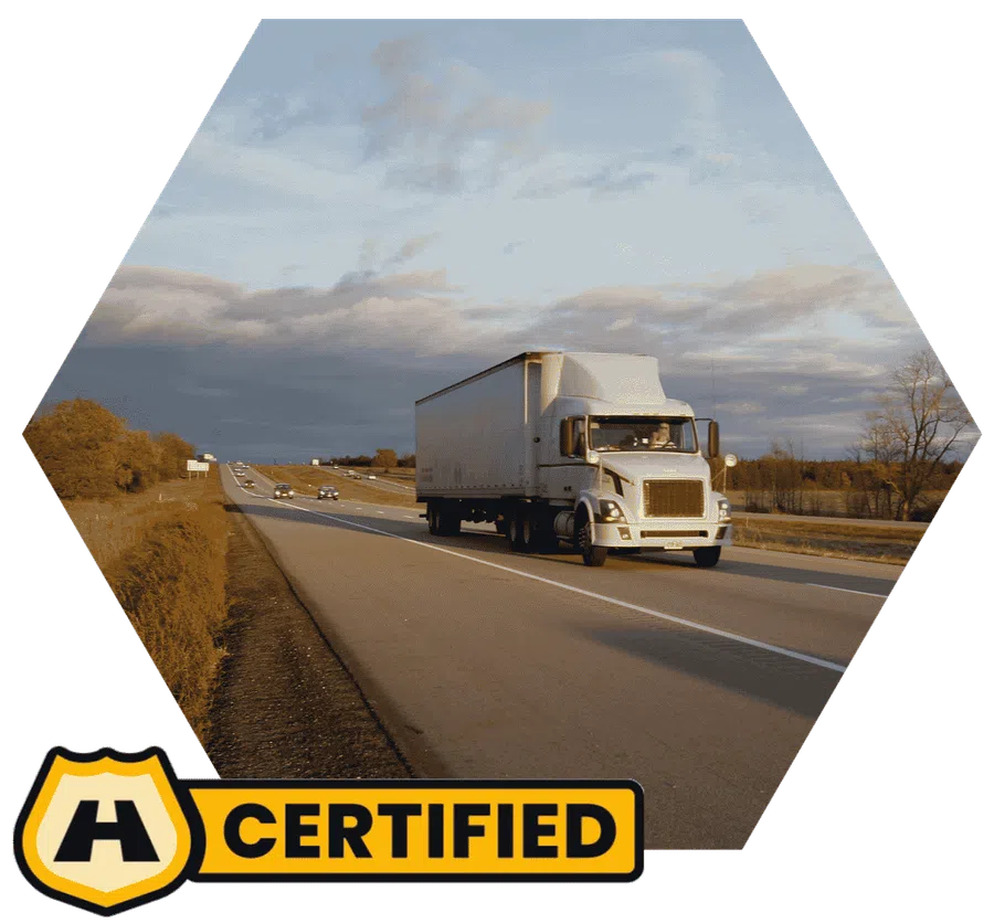 White semi truck driving on highway with cloudy sky in autumn landscape with certified badge overlay.