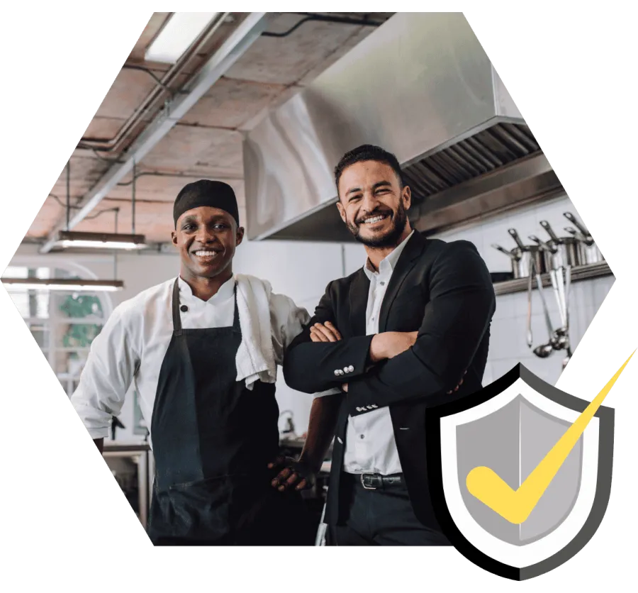 Two smiling men, one chef in uniform and one in business suit, standing in a modern kitchen setting.