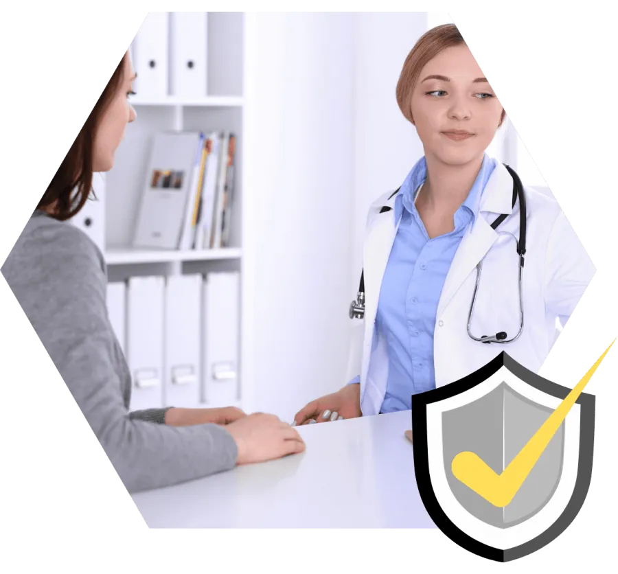 Female doctor in white coat consulting patient at medical office desk with bookshelf in background.