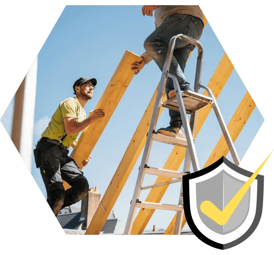 Two construction workers installing wooden beams on a roof under clear blue sky, one on ladder, one holding beam.